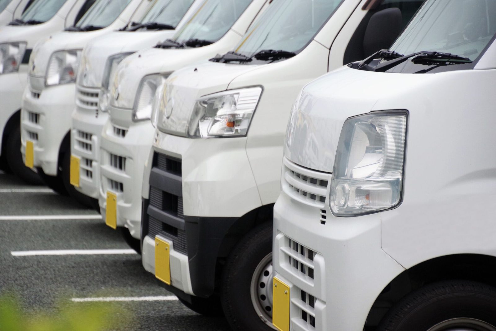 整列した白い商用バンの車列。用途に合わせて車種クラスを選べる法人レンタカーのイメージ
