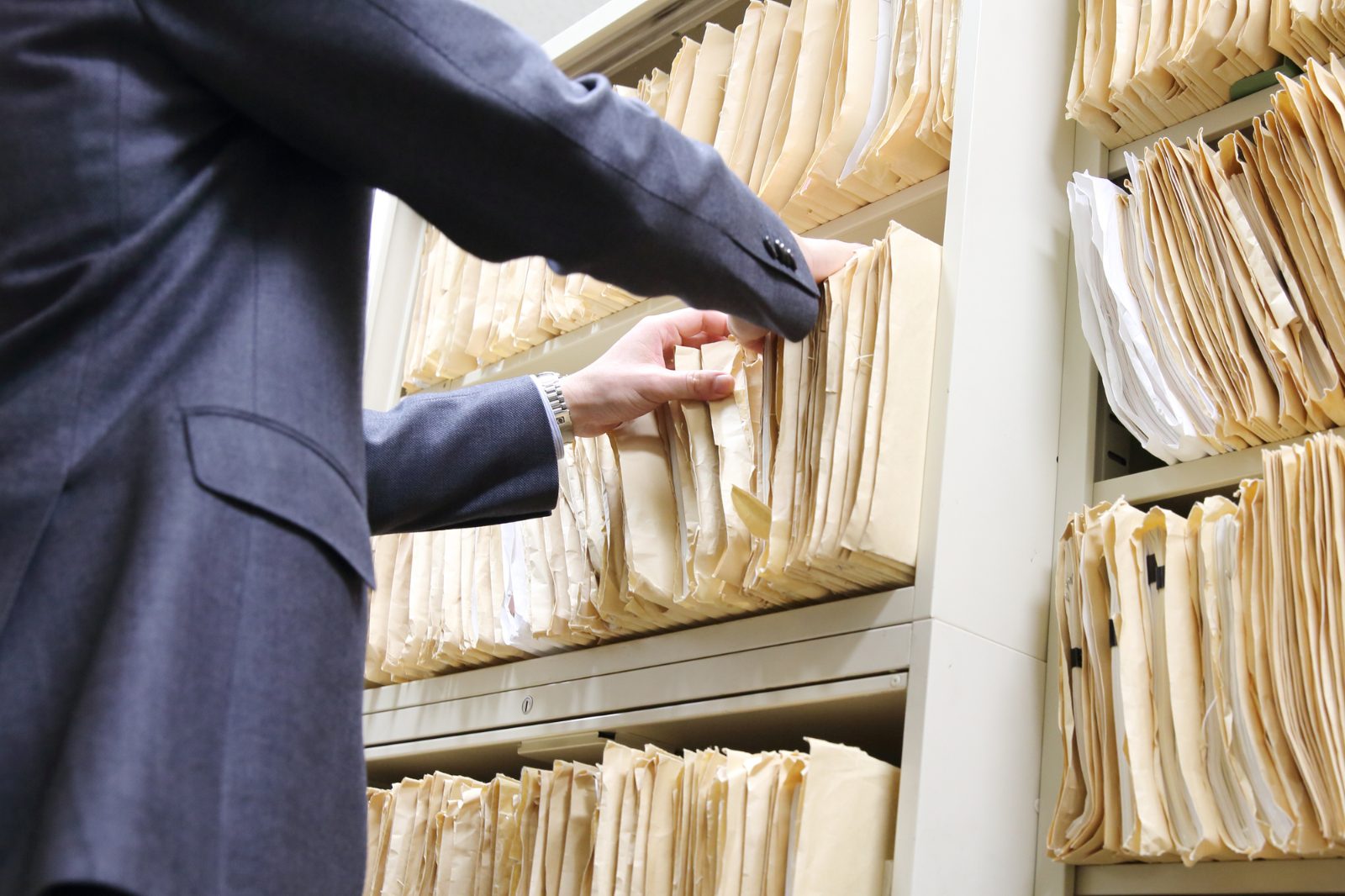 書庫のファイルから書類を探す手元。法人契約に必要な書類を事前に準備しておくイメージ