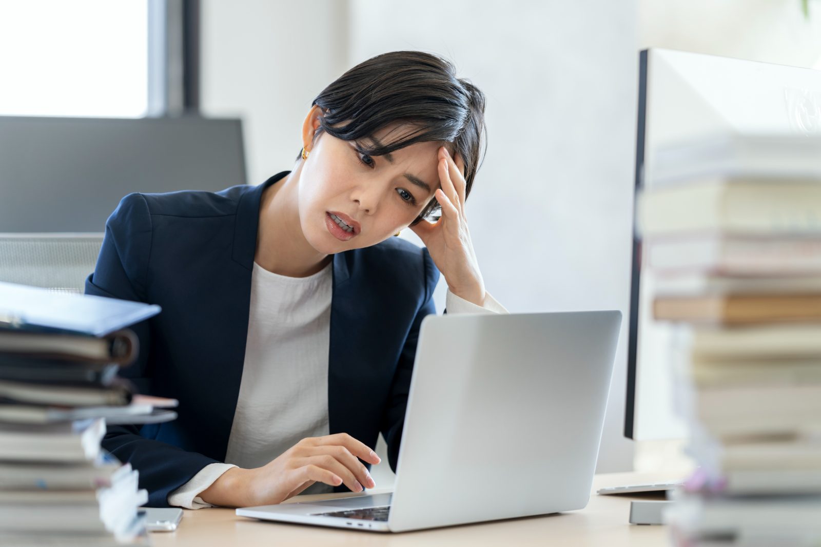 書類に囲まれたデスクで頭を抱える女性社員。車両不足で業務が回らない法人の状況イメージ