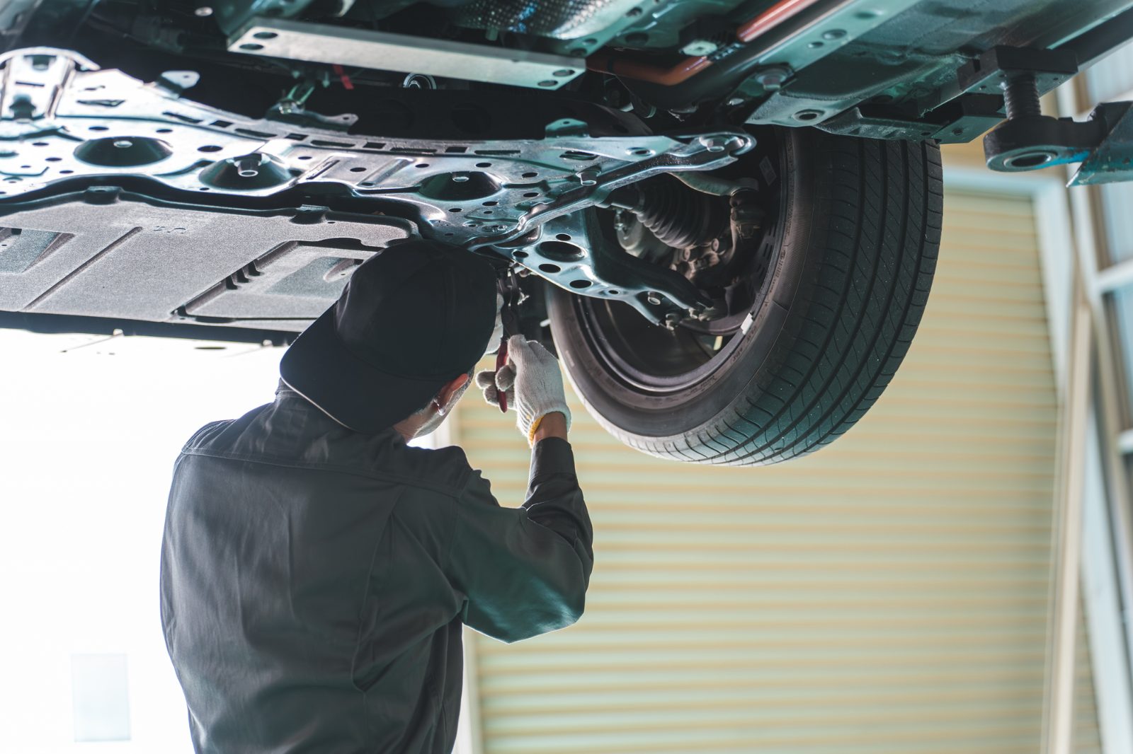 リフトアップした車の下回りを点検する整備士。レンタカーの整備・車検を貸主が管理するイメージ